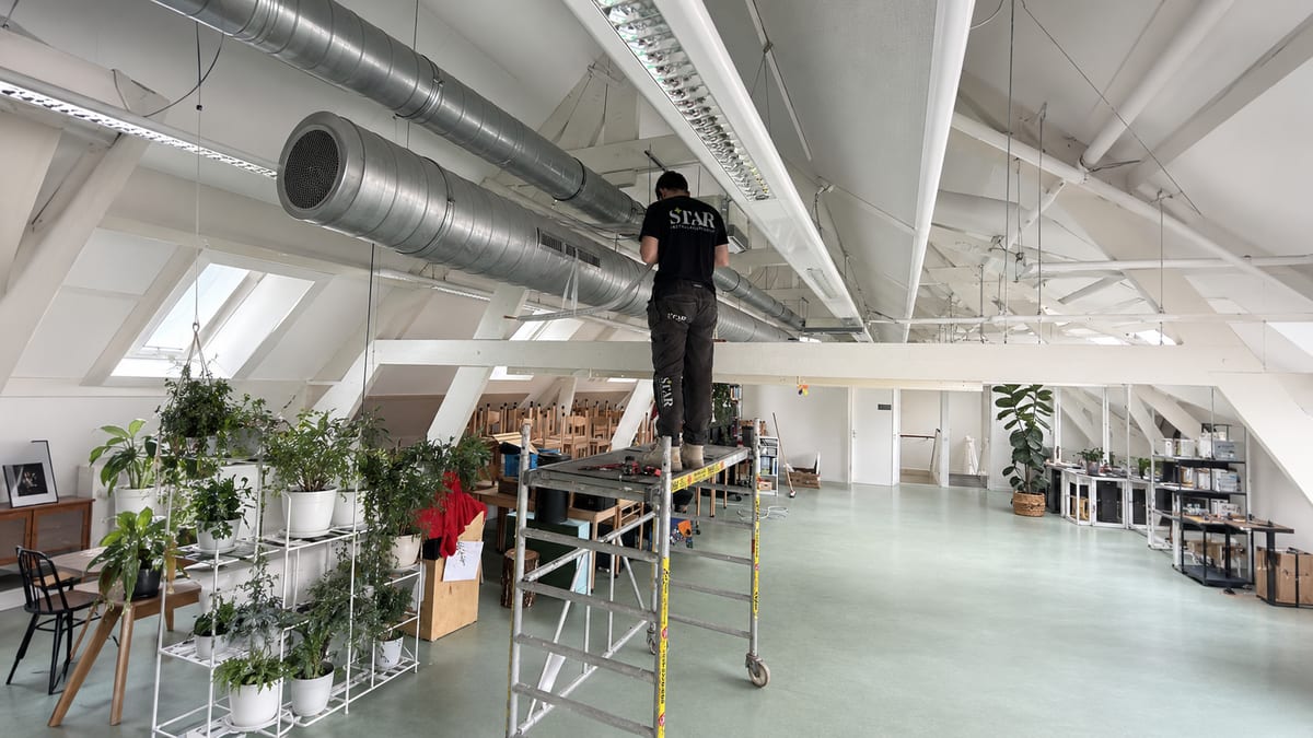 Monteur van Star Installatie installeert luchtkanalen in een lichte, moderne bedrijfsruimte